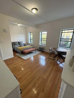 A room with a bed, a small table, a chair, and a radiator.