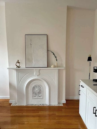 A room with a white fireplace, a framed artwork above it, and a cabinet to the right.. Brooklyn sleek studio apartment!