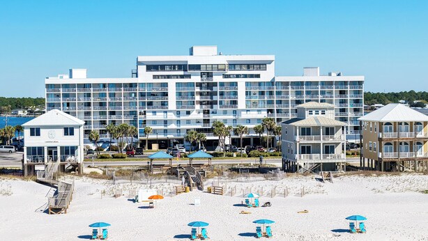 Un hotel frente a la playa con varios balcones, sombrillas de playa y un paseo marítimo que lleva a la arena.