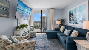 Una sala de estar con un sofá azul, un televisor de pantalla plana, un balcón con vistas y un cuadro de un pulpo.