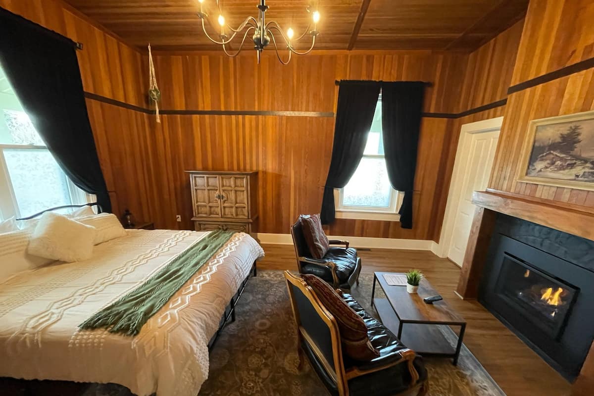 A cozy room with a bed, a leather sofa, a fireplace, and wooden paneling.