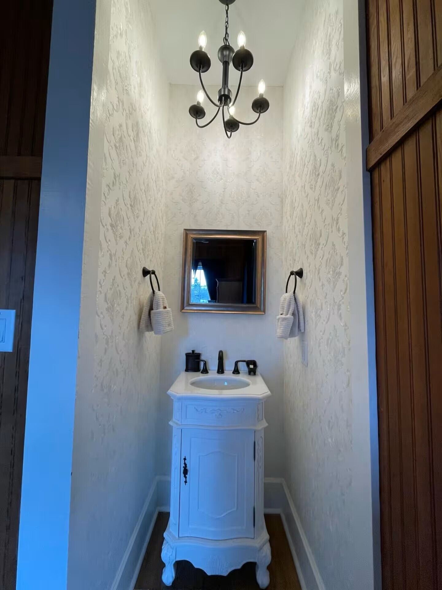 Een badkamer met een wit wastafelmeubel, een spiegel en een kroonluchter.