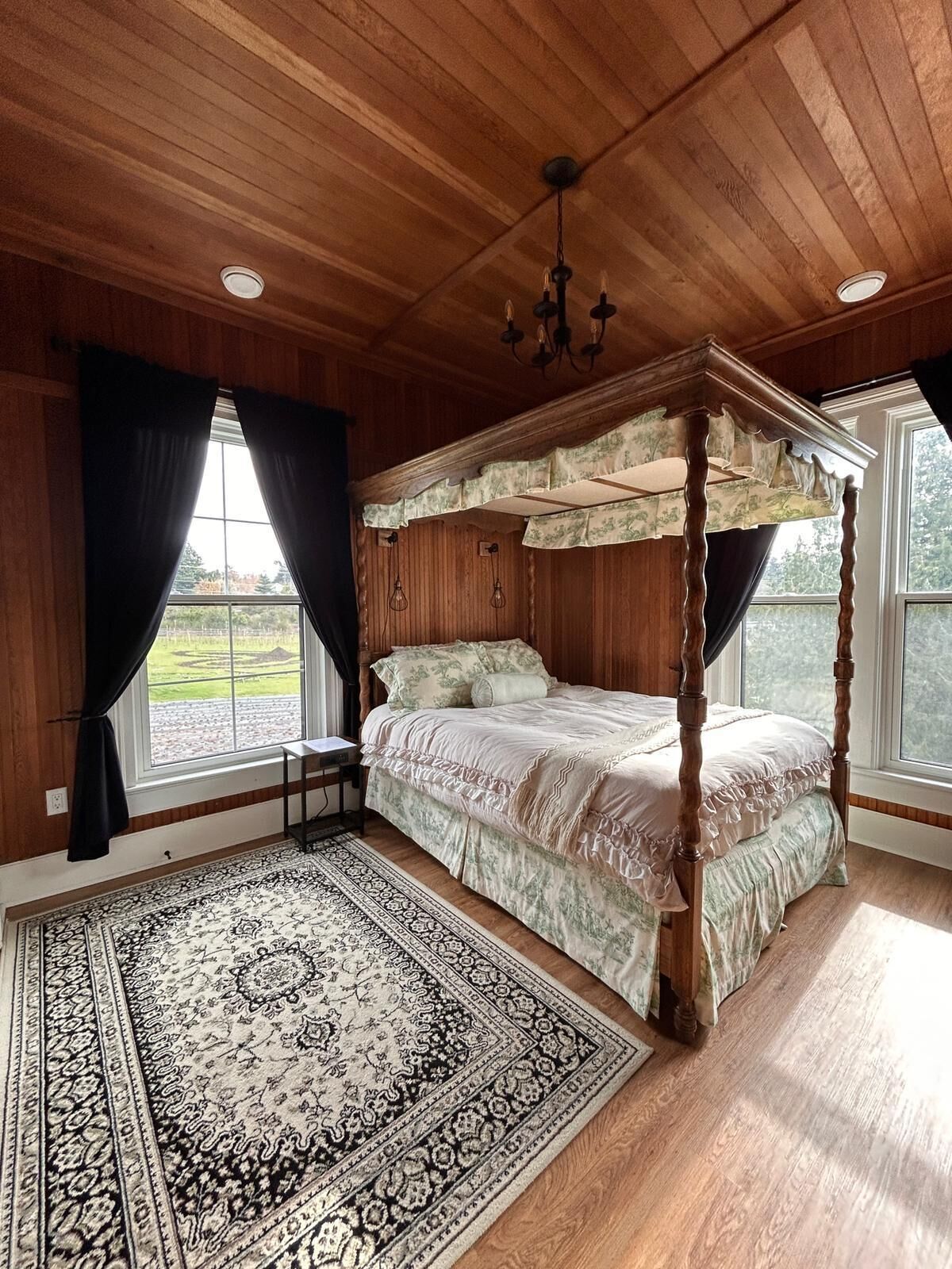 A four-poster bed in a room with wooden walls and a large window.
