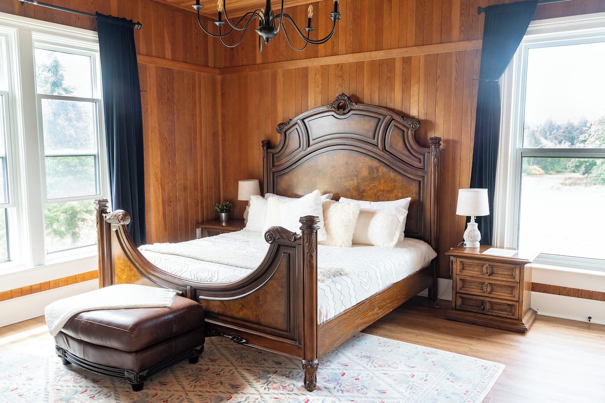 A wooden-paneled bedroom with a large bed, a nightstand, and a window with curtains.