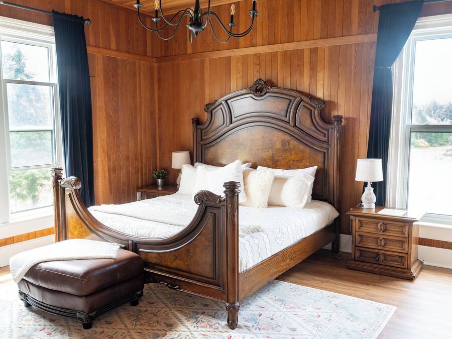 Un dormitorio con paneles de madera, una cama grande, una mesita de noche y una ventana con cortinas.