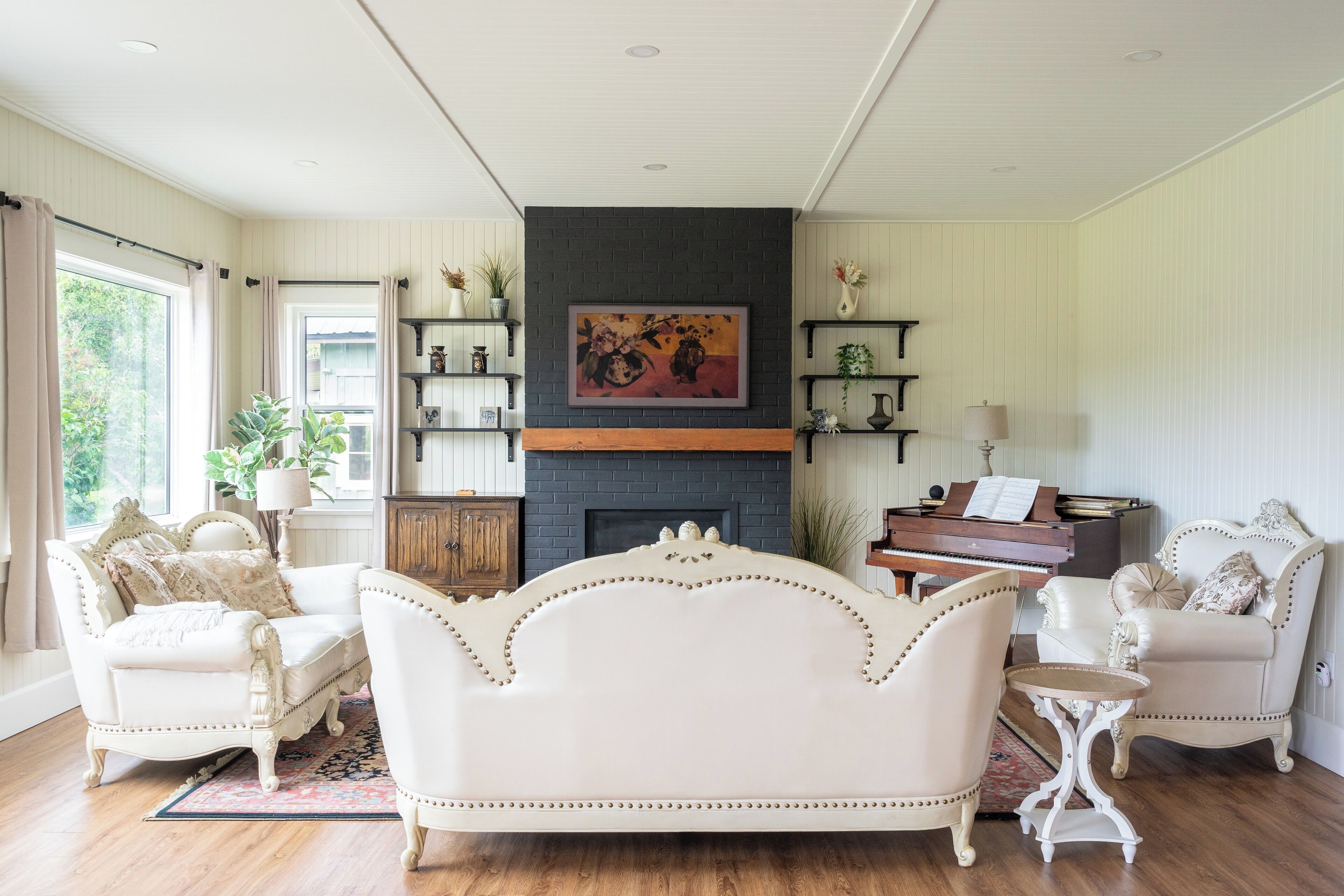 A living room with a fireplace, a piano, and two white armchairs.