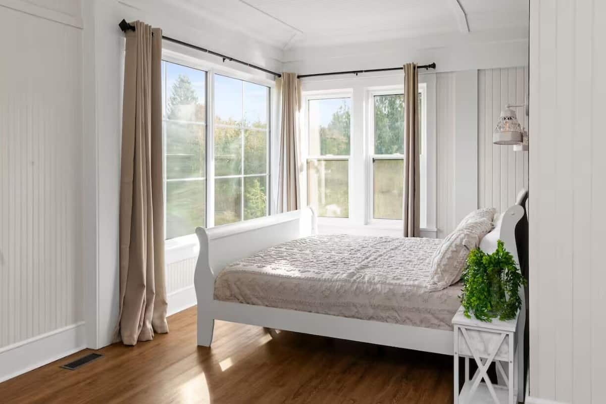 A bedroom with a bed, a window, and a nightstand with a plant.