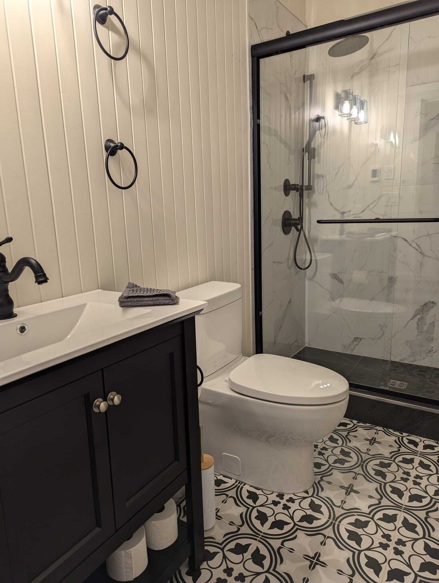 A bathroom with a white sink, dark cabinets, a toilet, and a glass shower enclosure.