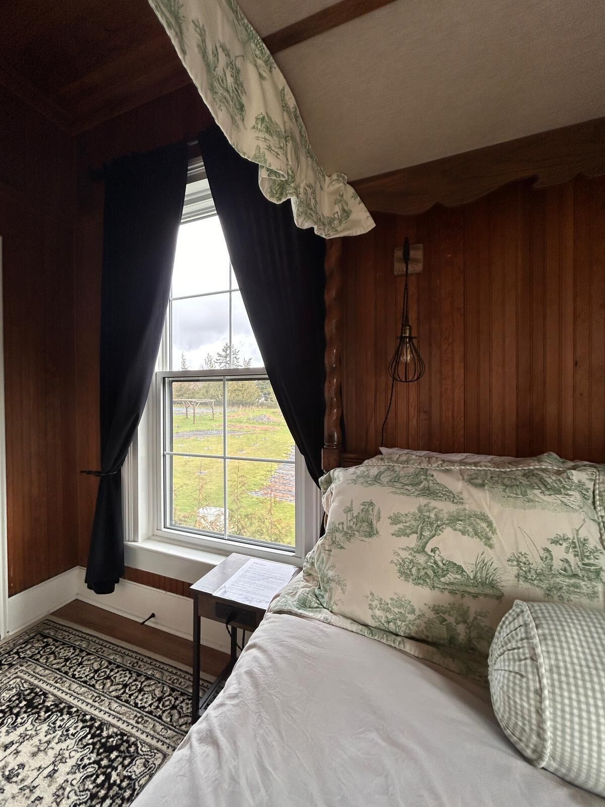 A bedroom with a bed, a window with curtains, a wooden ceiling, and a view of the outdoors.