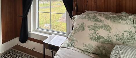 A bedroom with a bed, a window with curtains, a wooden ceiling, and a view of the outdoors.