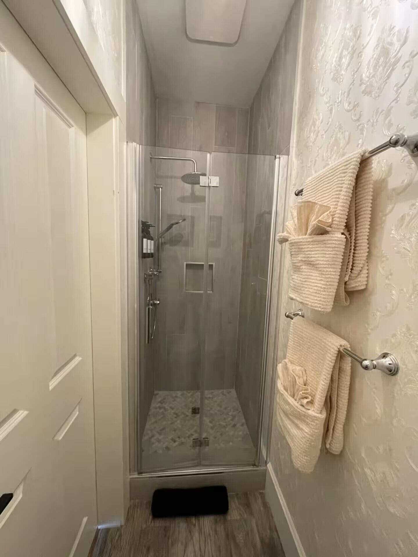 A glass-enclosed shower with a door, a towel rack with towels, and a patterned wall.