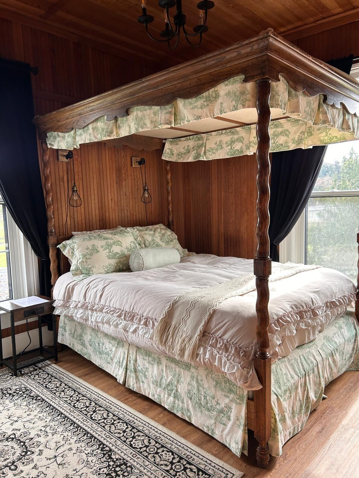Ein Bett mit Baldachin, mit Blumenmuster bezogen, ein Holzboden und ein Fenster mit Vorhängen.