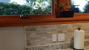A kitchen with granite countertops, two white plates, a roll of paper towels, and a window with a view of greenery. - Quality Luxury Apartment With Killer View & Double Studio (Bellevue)