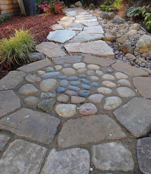 Un sendero de piedra con un diseño circular de piedras en el centro, rodeado de piedras más grandes y guijarros.