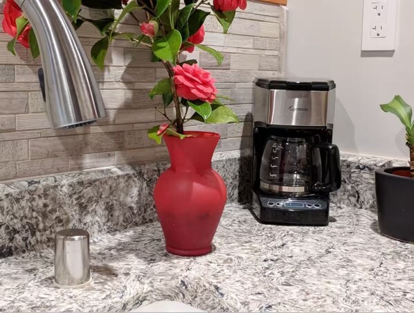 Una cocina con un jarrón rojo, cafetera y encimera de mármol.