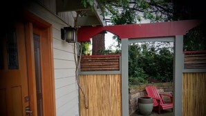 A covered patio area with a bamboo fence, a red chair, and a stone wall. - Quality Luxury Apartment With Killer View & Double Studio (Bellevue)