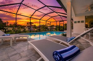 A poolside area with lounge chairs and a view of a sunset through a geometric glass structure.