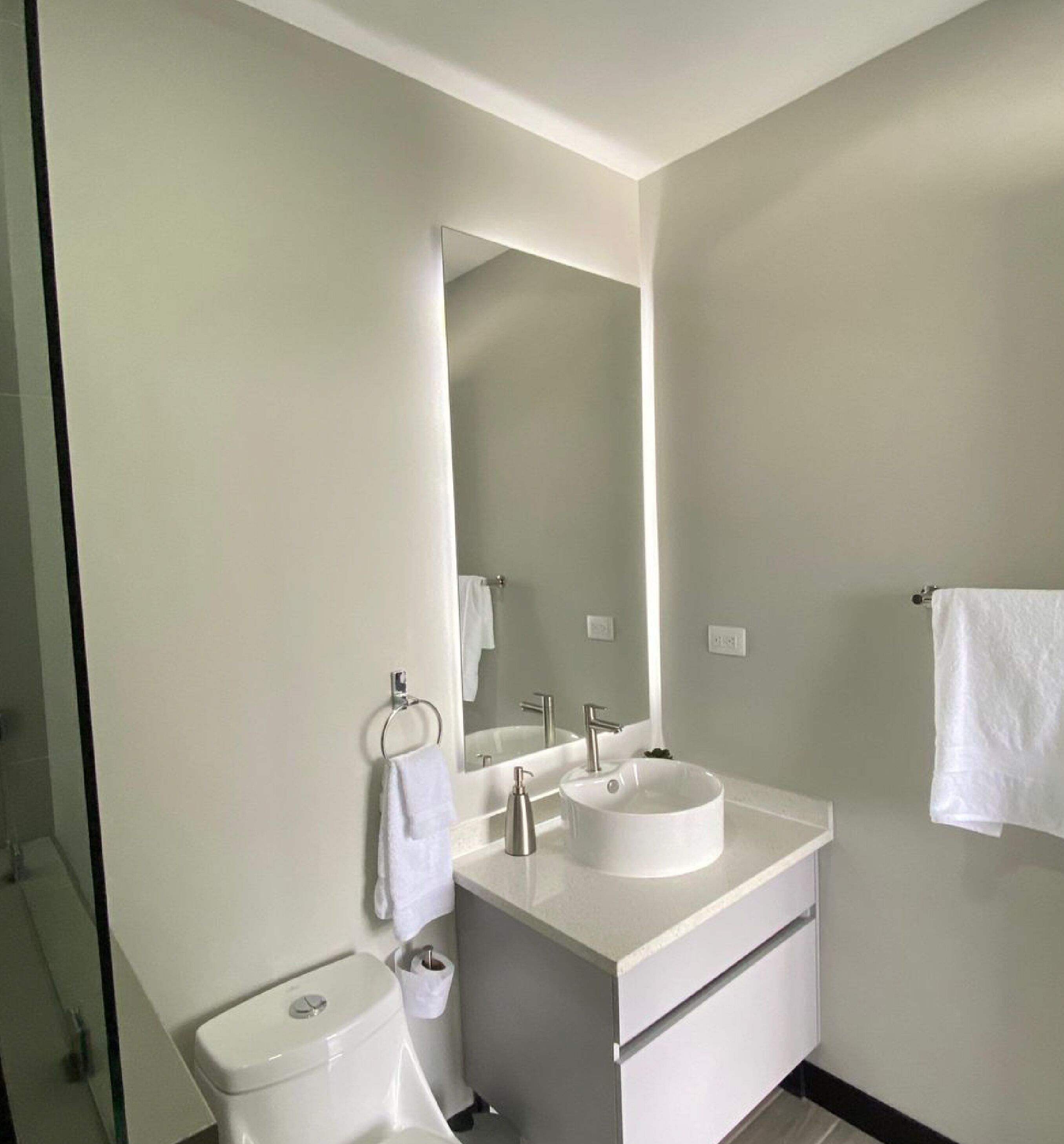 Un baño moderno con lavamanos, espejo e inodoro blancos.
