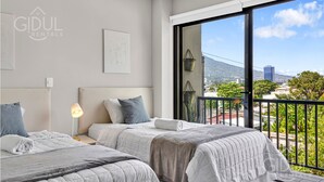 Een hotelkamer met twee bedden, een groot raam met uitzicht op de stad, en een balkon met een hekwerk.