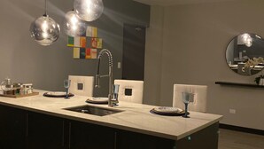 Een moderne keuken met een centraal eiland, hanglampen en een grote spiegel.