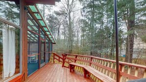 Eine Holzterrasse mit Bänken, einer Glastür und Blick auf ein bewaldetes Gebiet.