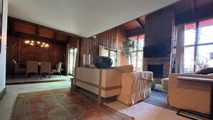 Ein gemütliches Wohnzimmer mit Kamin, Holzwänden und einem Essbereich mit Korbstühlen.
