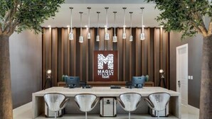 Ein Empfangsbereich mit modernem Design, der einen langen Empfandtisch, vier Stühle und ein an der Wand befestigtes Schild mit der Aufschrift "MAGIC IMAGE Resort" zeigt.