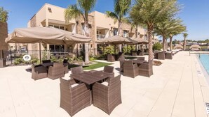 Ein Terrassenbereich im Freien mit Korbmöbeln und Sonnenschirmen, einem Pool und Palmen.