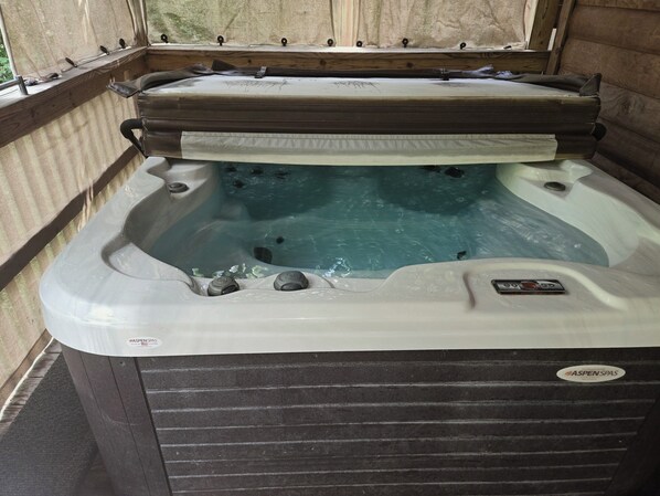 A hot tub with a control panel, a window with a view, and a wooden bench.