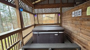 Een houten hut met een hottub, een houten terras en uitzicht op het omliggende bos.
