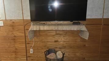 A room with a television mounted on a wooden wall, a woven shelf below, and a basket with rolled rugs on the floor.