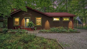 A wooden house with a red roof, a front porch with potted plants, and a gravel driveway. - HOT TUB, Sleeping Bear Dunes, M-22, Leelanau Wine Trail, Lake Michigan, TC (Cedar)