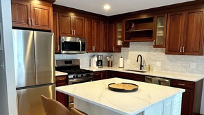 A modern kitchen with wooden cabinets, stainless steel appliances, a central island with stools, and a white countertop. - HOT TUB, Sleeping Bear Dunes, M-22, Leelanau Wine Trail, Lake Michigan, TC (Cedar)
