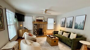 A living room with a green sofa, white armchair, and a wooden coffee table. There is a fireplace, a ceiling fan, and framed pictures on the wall. - HOT TUB, Sleeping Bear Dunes, M-22, Leelanau Wine Trail, Lake Michigan, TC (Cedar)