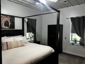 A four-poster bed with a headboard, a bedside table with a lamp, and a window with curtains.
