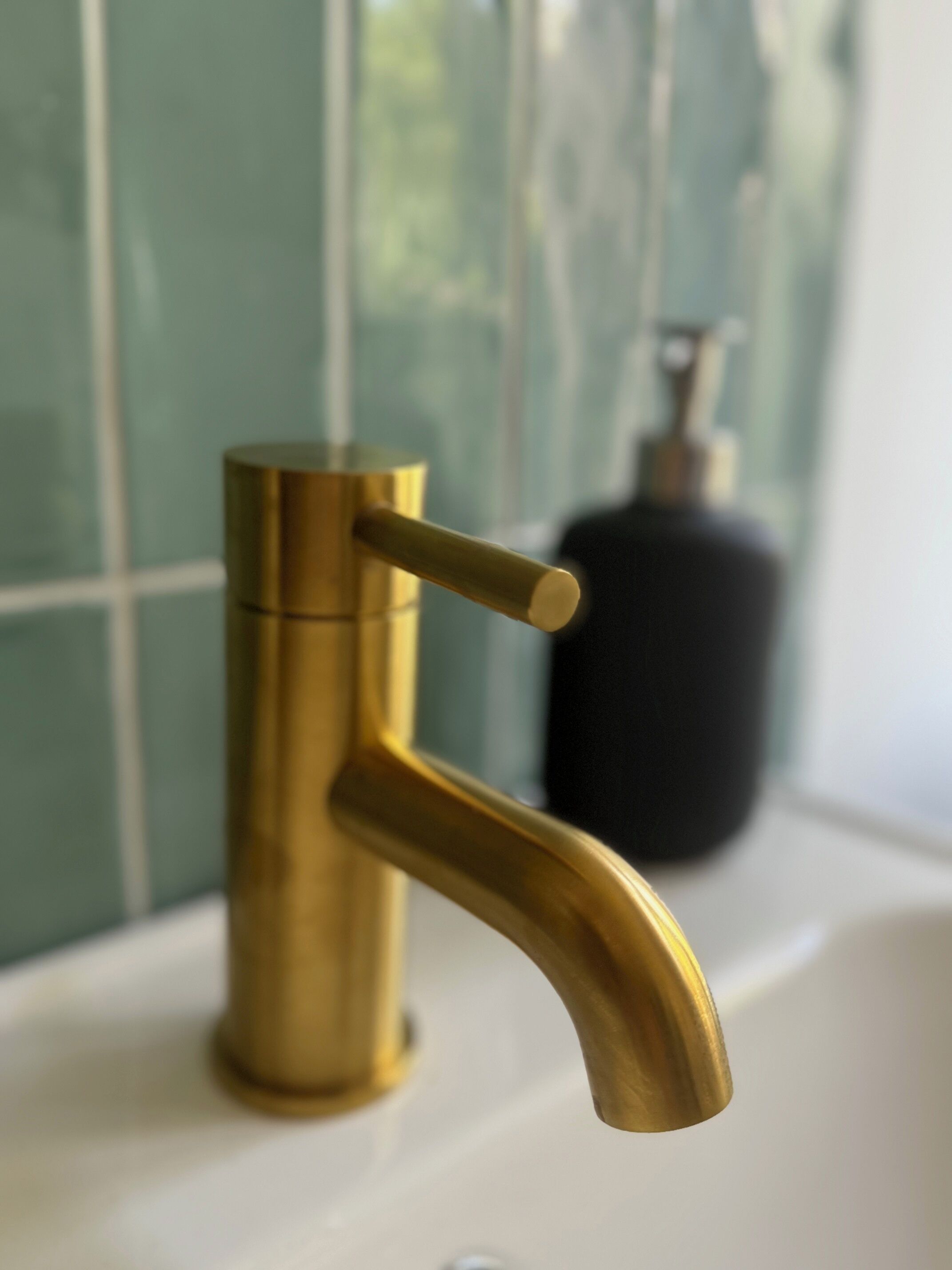 A bathroom with a gold faucet and a soap dispenser on the sink.