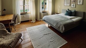 A bedroom with a bed, a desk, and a chair. There are curtains on the windows, and a hanging light fixture. - Beautiful apartment in a quiet location with good connections to Potsdam and Berlin (Potsdam)