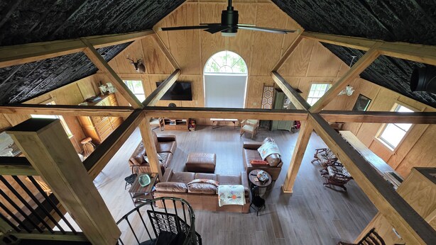 Amplia habitación tipo loft con techo alto, vigas de madera, una zona de estar central con sofá y sillones, una pequeña mesa y una escalera de caracol.