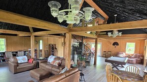 Amplia sala de estar con un sofá de cuero marrón grande, mesa de comedor de madera con sillas y una escalera que conduce a un nivel superior.