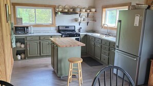 Una cocina con vigas de madera, una isla central, armarios verdes y un refrigerador.