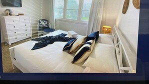 Een slaapkamer met een bed, een dressoir, een stoel, een raam en een lamp.