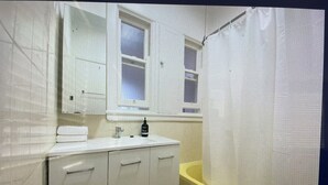 Een kleine, compacte badkamer met een wit wastafel, spiegel en een bad met een gele rand.
