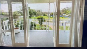 Een balkon met uitzicht op een groen park en een weg.