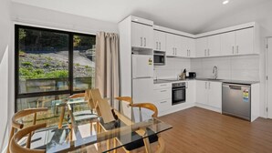 Una cocina moderna con armarios blancos, una mesa de comedor de vidrio y vistas al exterior.