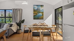 Una sala de estar moderna con una mesa de comedor de vidrio, sillas de madera, un sofá y un ventanal con vistas a zonas verdes y montañas.