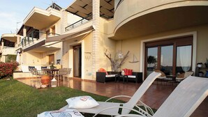 Une vaste terrasse extérieure dotée de chaises longues et d’un espace repas, agrémentée d’une grande fenêtre et d’une branche d’arbre décorative.