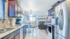 A modern kitchen with stainless steel appliances, a marble countertop, and a dining area with a white chair. - Pine & Peak - Bright, Airy Home w/ Big Views in Peaceful Family Area (Colorado Springs)