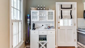 A kitchen with white cabinets, a coffee maker, and a wine bottle on the counter. - RVA Old Willow Bungalow | Quaint & Quiet | 2 Kings (Richmond)