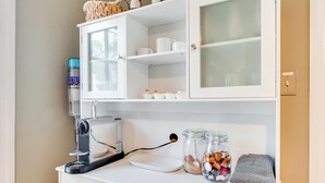 A kitchen with a coffee machine, jars of spices, and a cabinet with glass doors. - RVA Old Willow Bungalow | Quaint & Quiet | 2 Kings (Richmond)