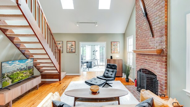 A spacious living room with a wooden staircase, a fireplace, and a television on a wooden console. - RVA Old Willow Bungalow | Quaint & Quiet | 2 Kings (Richmond)